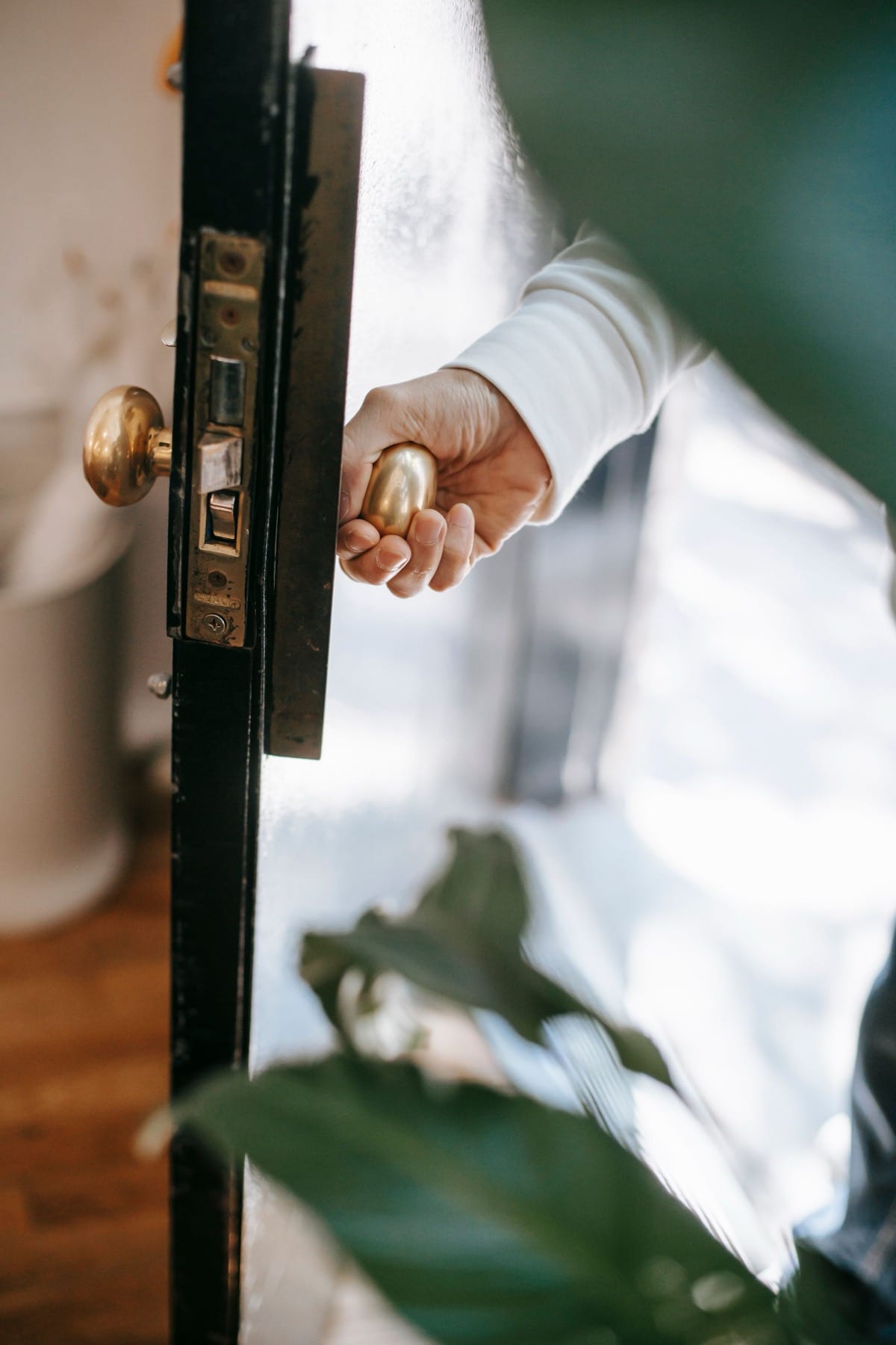 A hand on a brass door handle, letting themselves into a sunlit home