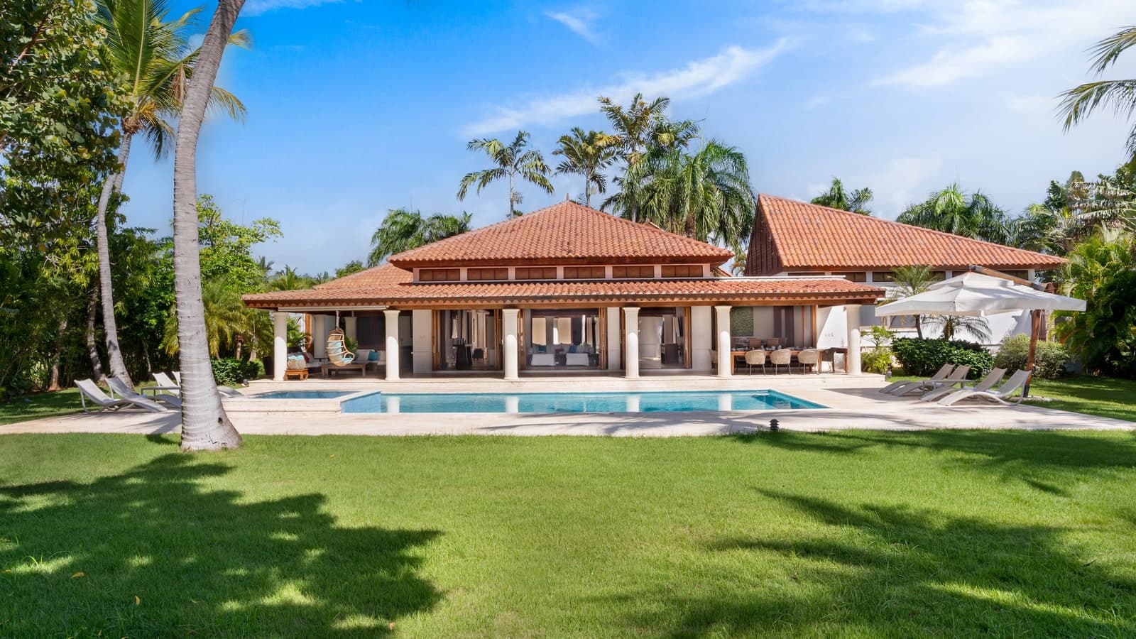 A villa with a terracotta roof, its pool and lawn framed by palm trees