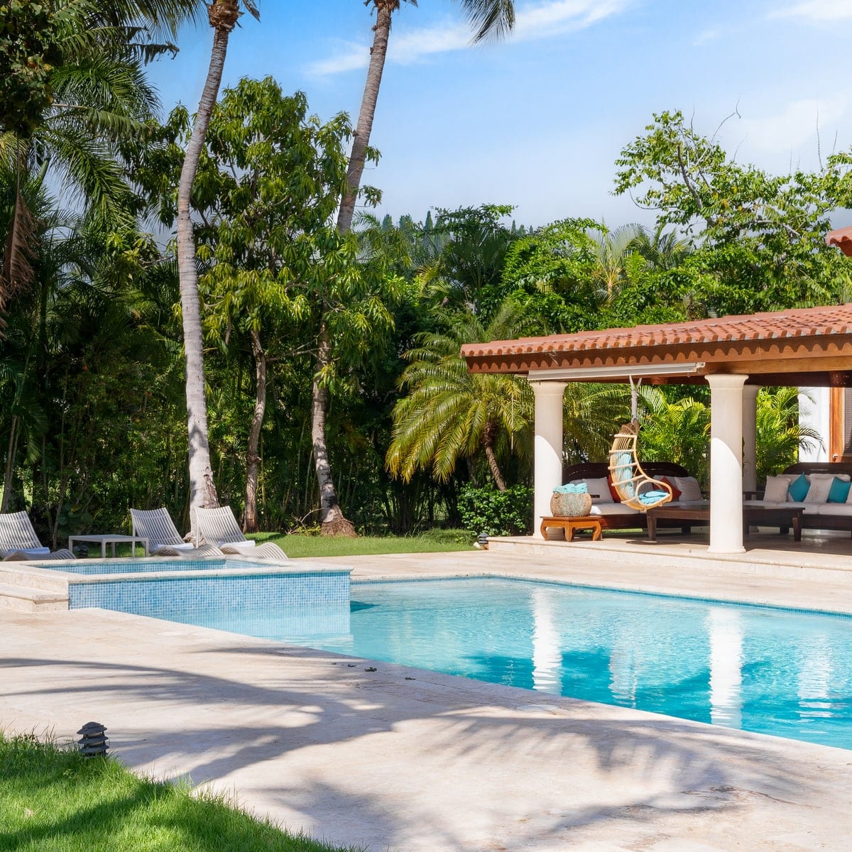 A villa's pool and covered terrace under palm trees